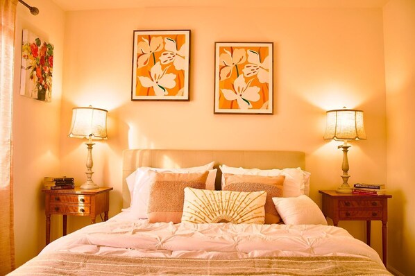 A bedroom with a large bed, two bedside tables, two lamps, and two framed floral artworks on the wall. - Charming 4bd house near the coast with backyard (Oxnard)