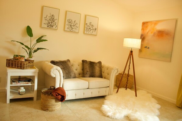 A living room with a white sofa, three framed floral artworks, a floor lamp, and a fluffy white rug.