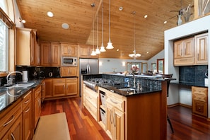 A modern kitchen with wooden cabinets, a central island, stainless steel appliances, and pendant lighting.