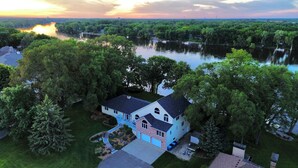 A two-story house with a front porch, surrounded by lush greenery and a river.