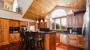 A spacious kitchen with wooden cabinets, a central island with bar stools, a stainless steel refrigerator, and a large window providing natural light.