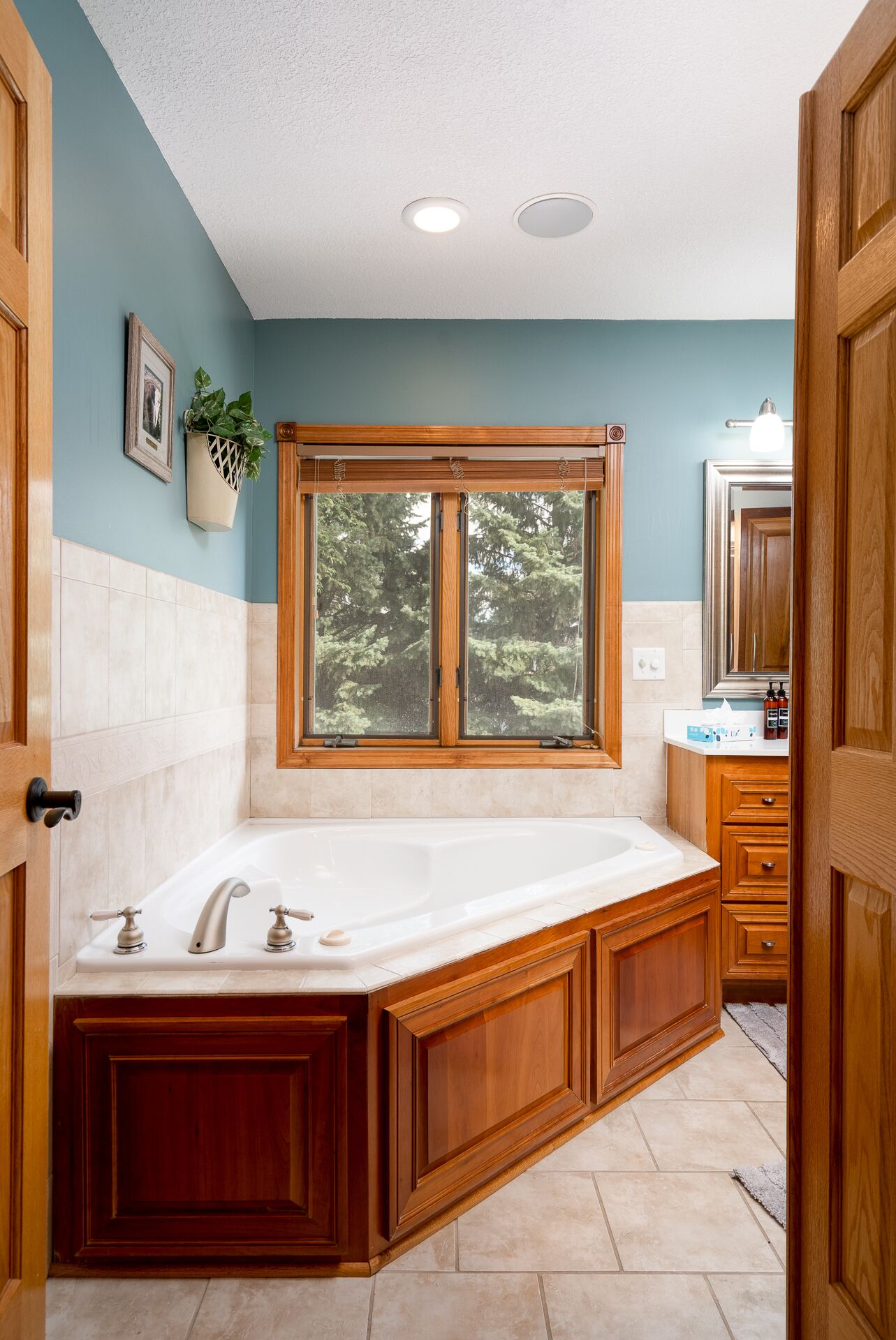 A bathroom with a large wooden vanity, a freestanding bathtub, and a window with a view of trees.