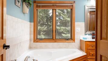 A bathroom with a large wooden vanity, a freestanding bathtub, and a window with a view of trees.