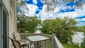 A balcony with a table and chairs overlooking a lake, surrounded by trees.
