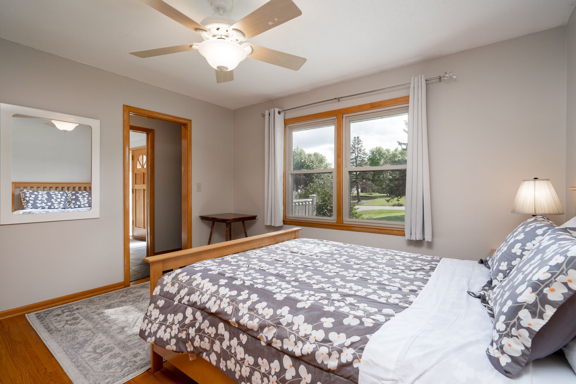 A bedroom with a bed, a ceiling fan, a window with curtains, and a view of the outdoors.