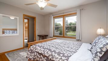 A bedroom with a bed, a ceiling fan, a window with curtains, and a view of the outdoors.