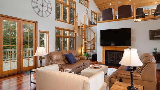 A spacious living room with a large TV, comfortable seating, and a wooden staircase.