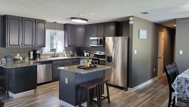 A modern kitchen with dark cabinetry, stainless steel appliances, and a central island with stools. - Great Gulf Breeze Getaway Near Pensacola Beach (Gulf Breeze)
