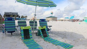 Beach chairs with striped cushions and a striped towel laid out on the sand, a striped umbrella, and a building in the background. - Great Gulf Breeze Getaway Near Pensacola Beach (Gulf Breeze)