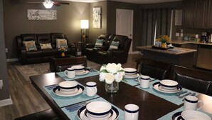A dining area with a table set for four, surrounded by dark leather sofas and a kitchen in the background. - Great Gulf Breeze Getaway Near Pensacola Beach (Gulf Breeze)