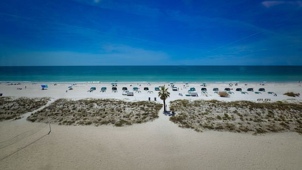 A beach with tents and umbrellas, a clear sky, and a sandy path leading to the water. - Beautiful Beach View Condo with heated pool. No Resort Fees. (Treasure Island)