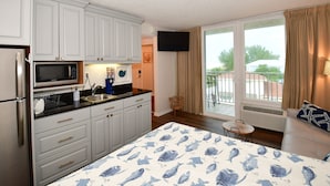 A hotel room with a kitchen area, a bed with a blue and white fish pattern bedspread, a TV mounted on the wall, and a balcony with a view of the outside. - Beautiful Beach View Condo with heated pool. No Resort Fees. (Treasure Island)