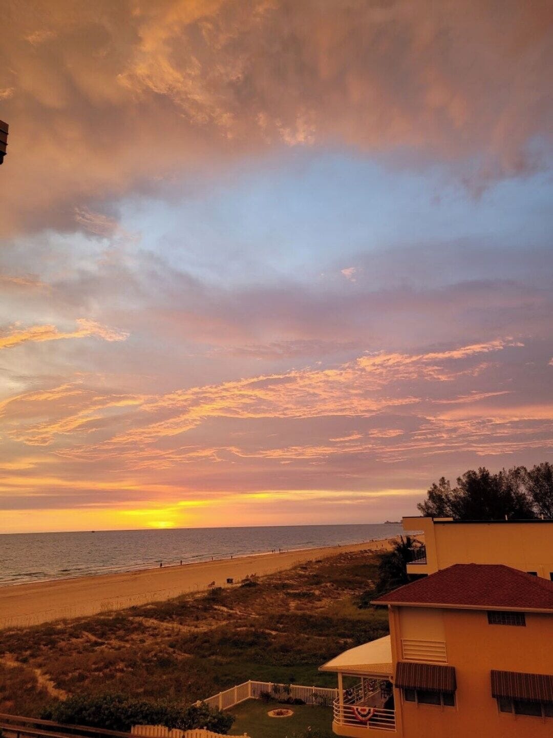 Vista costera con playa, un edificio de techo rojo y cielo nublado.