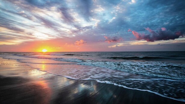 Ein Strand mit Wellen bei Sonnenuntergang, blauem Himmel und ruhiger See.