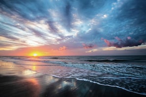 Ein Strand mit Wellen bei Sonnenuntergang, blauem Himmel und ruhiger See.