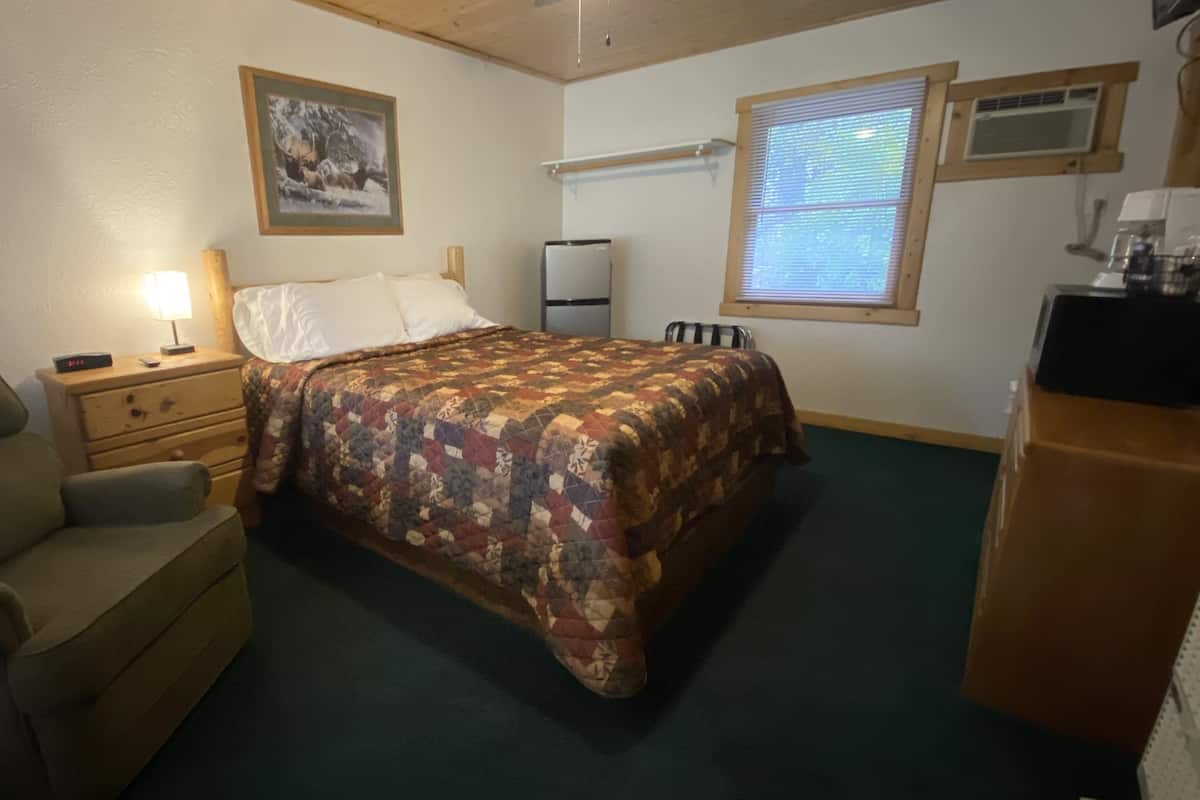 Una camera da letto con un letto, una sedia, un comodino, una cassettiera, una finestra e un quadro appeso al muro.