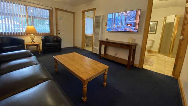 Ett vardagsrum med ett soffbord i trä, en svart lädersoffa, en tv som är monterad på väggen och en öppen spis.