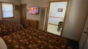 Ett rum med två sängar, en tv, en byrå och en dörr som leder till ett annat rum.