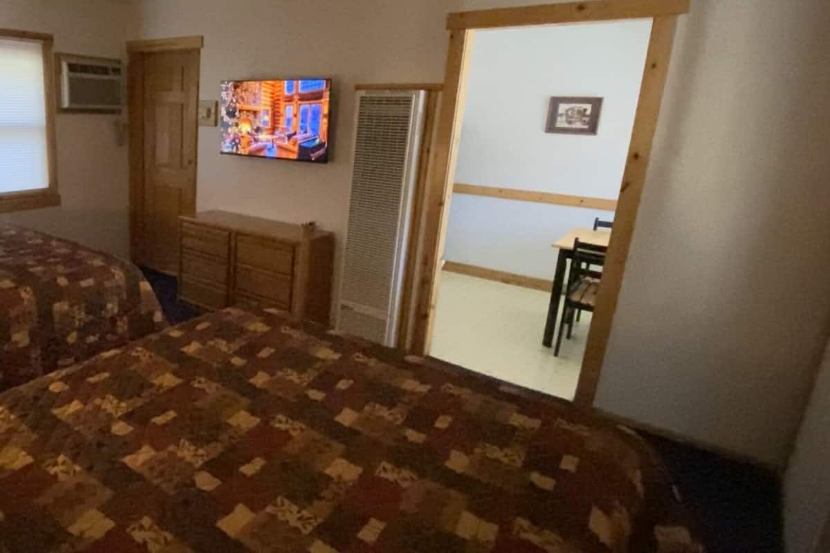 Una stanza con due letti, una televisione, una cassettiera e un ingresso verso un'altra stanza.
