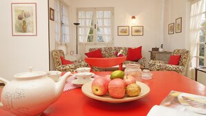 Una sala de estar acogedora con una mesa roja, sillones estampados y una tetera blanca sobre la mesa.