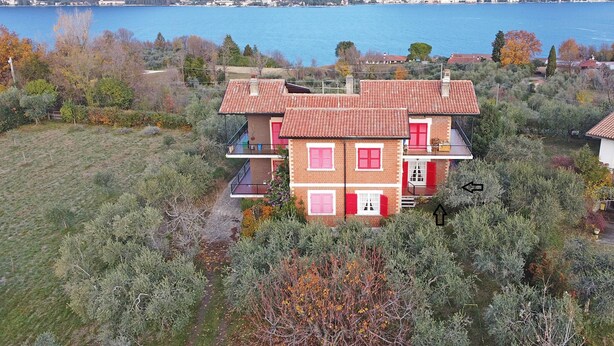 Una casa de dos pisos con techo de tejas rojas, rodeada de árboles y vistas al lago.