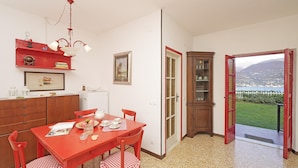Un comedor con una mesa y sillas rojas, un refrigerador blanco, un armario de madera y vistas a través de una puerta abierta.