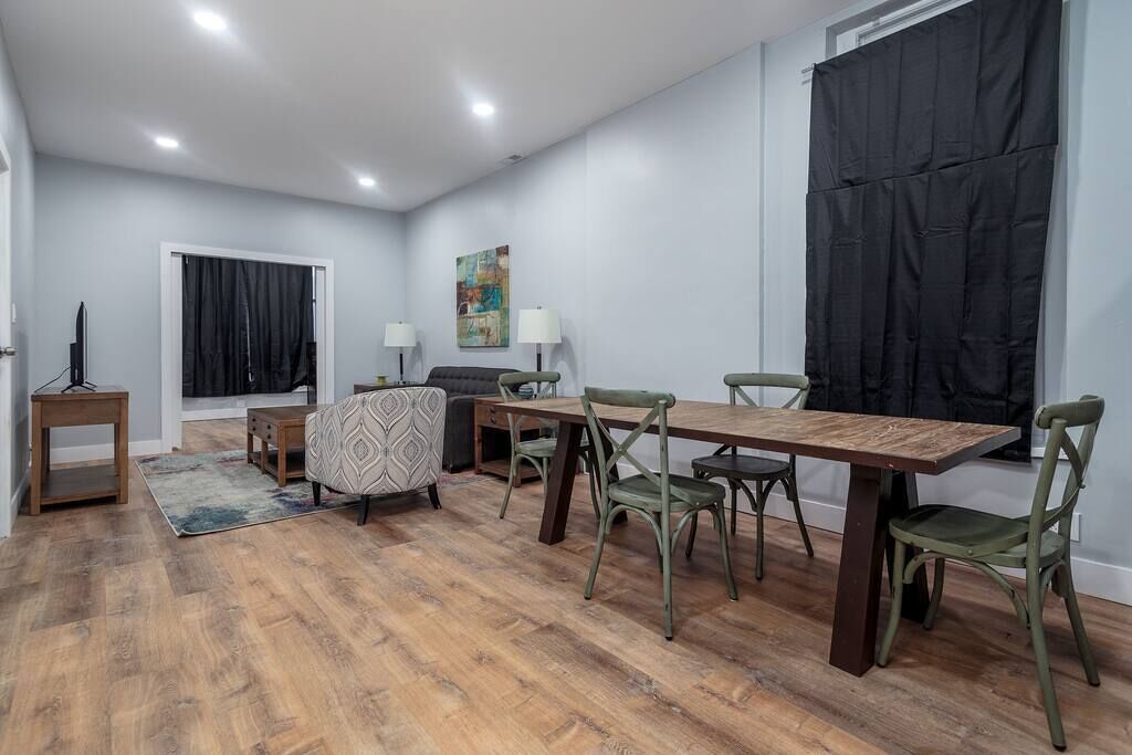 Een moderne woonkamer met een houten eettafel, groene stoelen, een gestreept bankstel en een schilderij aan de muur.