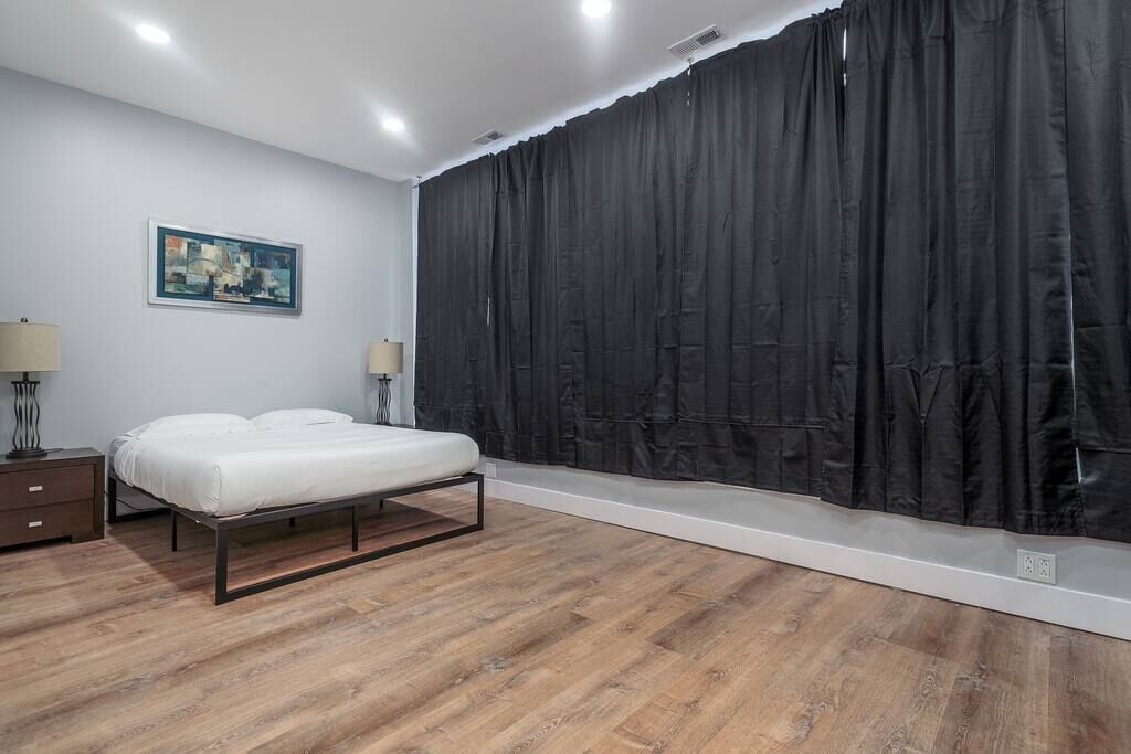 Een slaapkamer met een bed, twee nachtkastjes, een schilderij aan de muur en een groot zwart gordijn.