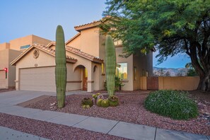 A house with a garage, a driveway, and a garden with cacti and a tree.
