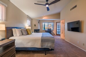 A bedroom with a bed, a desk, a TV, and a ceiling fan.