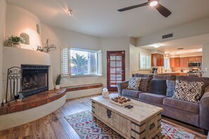 A living room with a fireplace, a sofa, a coffee table, and a view of the kitchen.