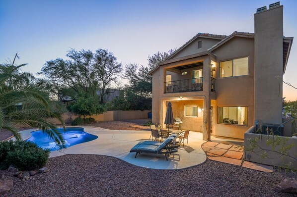 A two-story house with a backyard featuring a swimming pool, outdoor seating, and a barbecue area.