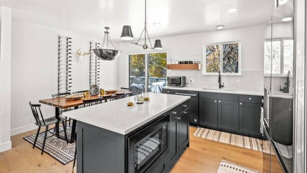 Una cocina moderna con una isla central, armarios oscuros e iluminación colgante.