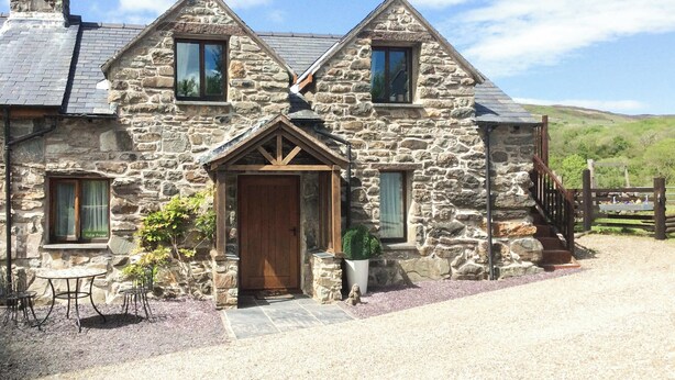A stone house with a wooden door, a small porch, and a gravel driveway. - 1 bedroom accommodation in Blaenau Ffestiniog (Blaenau Ffestiniog)