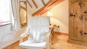 A cozy room with a wooden ceiling, a white cushioned chair, a wooden cabinet, and a lamp. - 1 bedroom accommodation in Blaenau Ffestiniog (Blaenau Ffestiniog)