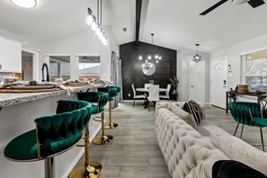Une cuisine moderne avec un coin repas, comprenant un bar avec des tabourets en velours vert, un canapé capitonné et un mur d’accent noir.