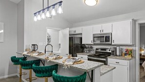 A modern kitchen with white cabinets, a central island with bar stools, a stainless steel refrigerator, and a microwave.