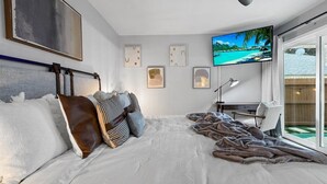 A bedroom with a large bed, a desk, and a TV displaying a tropical beach scene.