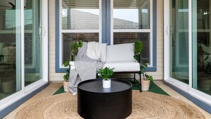 A modern outdoor seating area with a black round table, two white sofas, and potted plants.