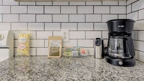 Un taulell de cuina amb una cafetera, un sac de crispetes, una caixa de cereals i un molinet de cafè.