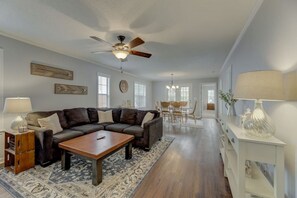 A spacious living room with a dark brown sectional sofa, a wooden coffee table, and a ceiling fan. There is a dining area with a wooden table and chairs, and a white console table with a lamp. - Walk Lex & Main St | Near Old Mill Brew Pub | 3BR (Lexington)