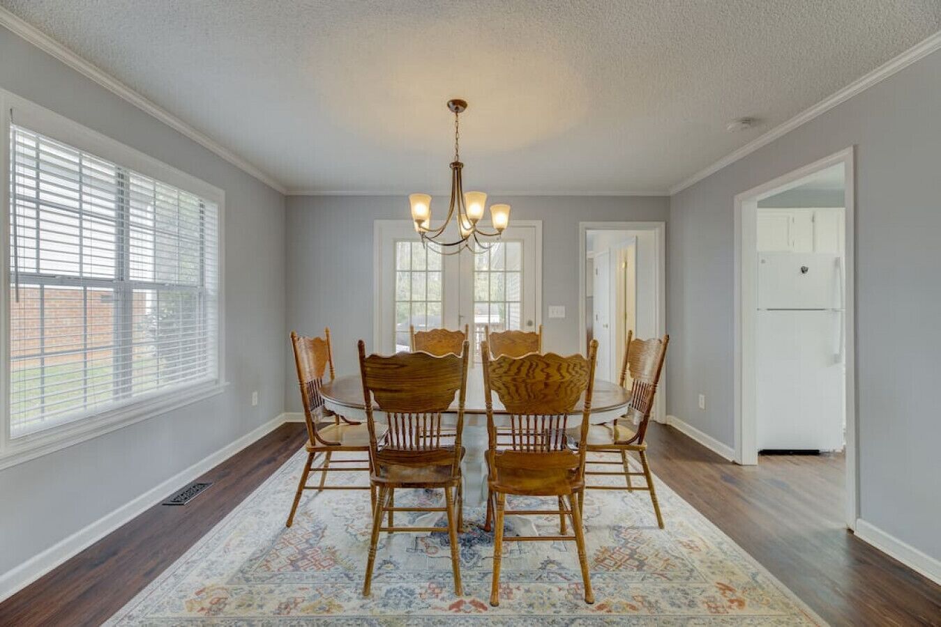 A dining room with a chandelier, wooden chairs, and a patterned rug.