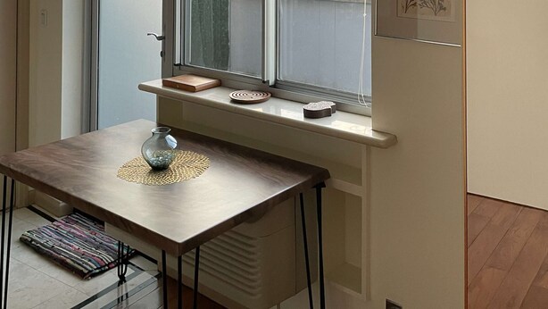 A modern apartment with a large window, a dining table with a placemat, and a flat-screen TV mounted on the wall. - Stylish studio apartment in the heart of East Harlem (New York)