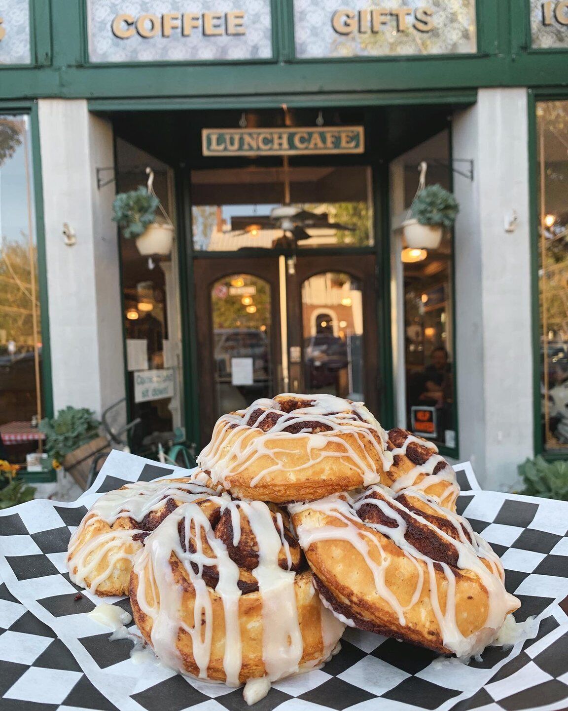 A stack of cinnamon rolls with icing in front of a coffee and gift shop.