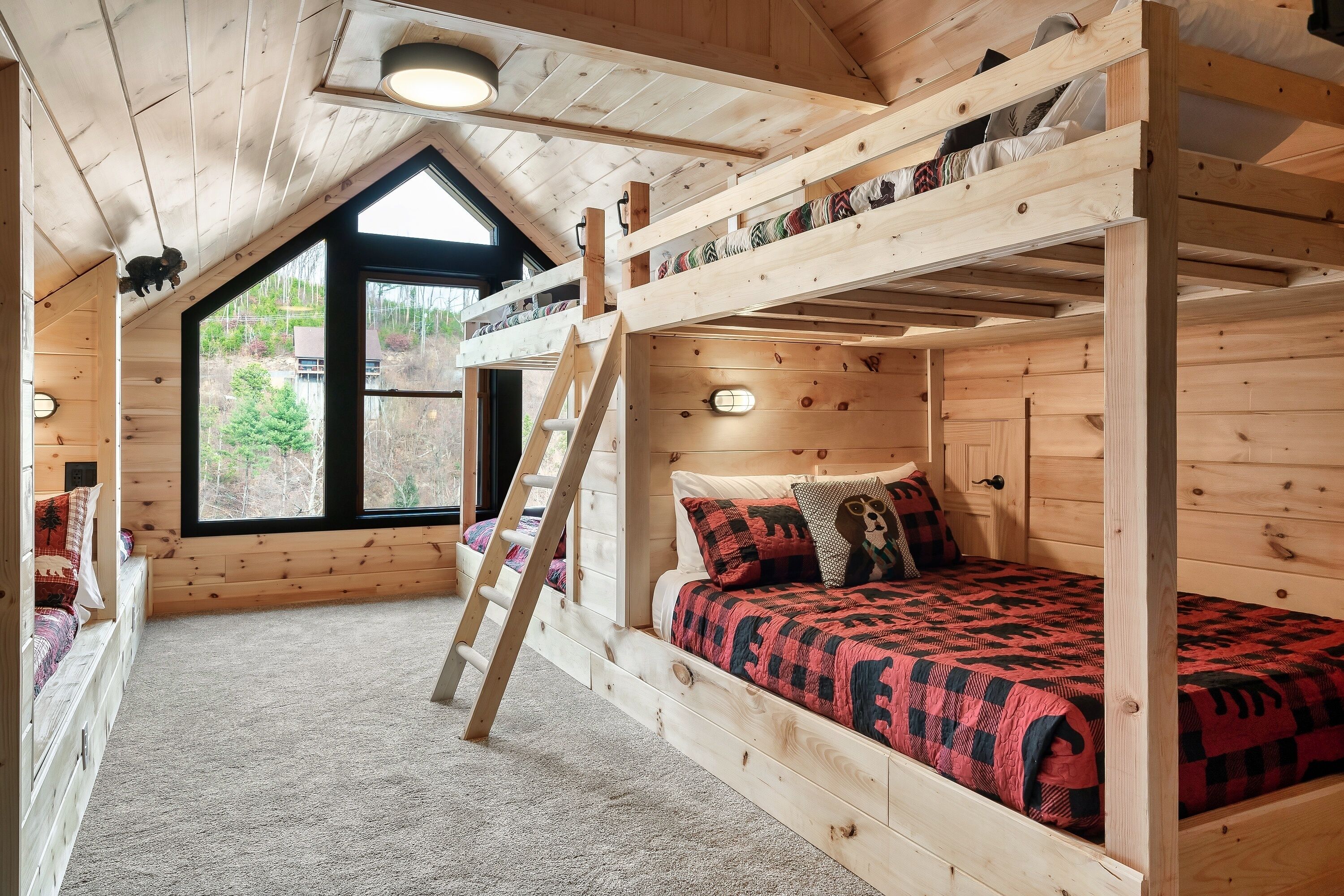 Una cabaña de madera con cama en un altillo, una escalera y un ventanal con vistas al exterior.