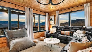 Una sala acogedora con un sofá de cuero, un ventanal con vistas a la montaña y paredes de madera.