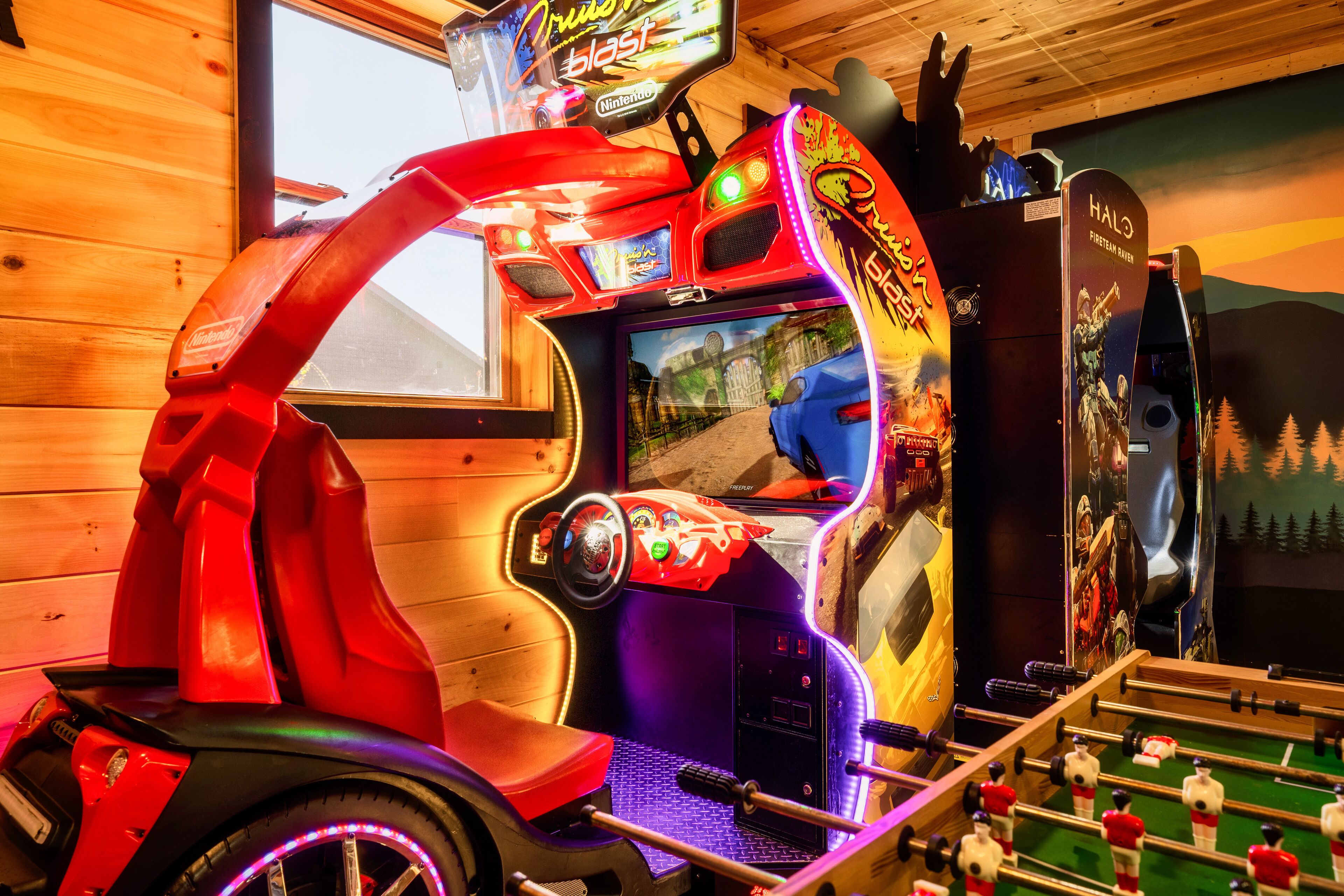 A video game arcade with a racing game, a foosball table, and a mural on the wall.