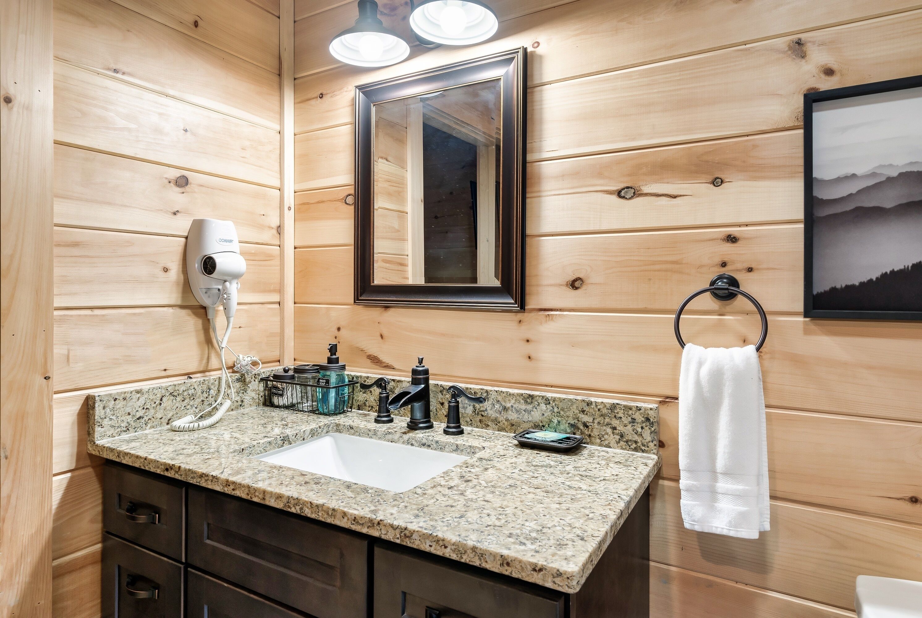 A wooden cabin bathroom with a granite countertop, a sink, a hairdryer, a mirror, and a towel ring.