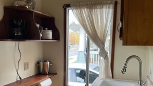 Une cuisine compacte comprenant un évier, une fenêtre avec des rideaux et une étagère avec des appareils de cuisine.