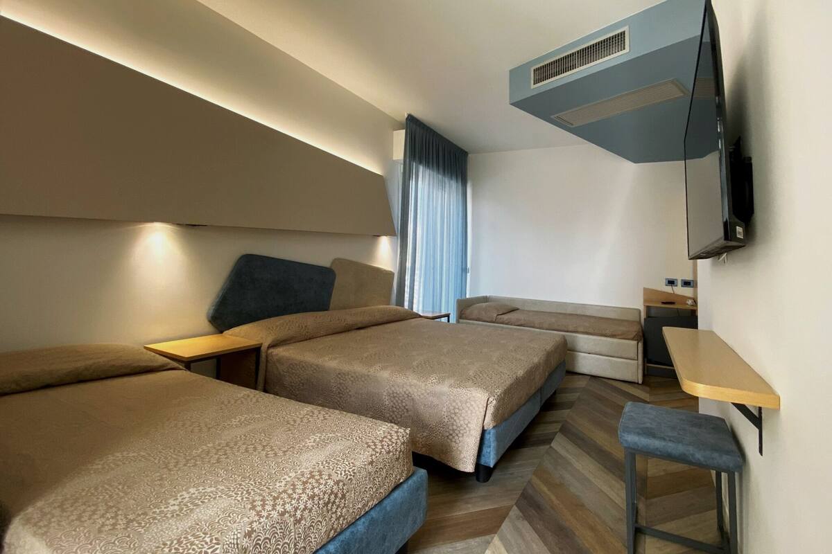 A hotel room with two beds, a desk, a chair, a TV, and a window with curtains.